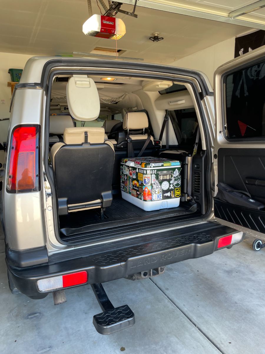 The family's green Coleman cooler covered in outdoor stickers, loaded in the back of a Land Rover